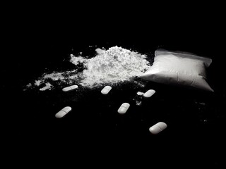 Cocaine drug powder pile ang bag and pills on black background