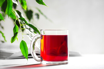 A mug with red tea on a light gray background, a book lies next to it, horizontal orientation, copy space