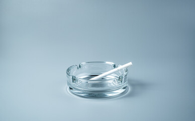 A cigarette in a transparent ashtray on a gray background. Side view with copy space. The concept of the harm of smoking.