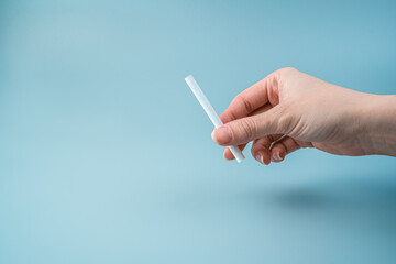 A woman's hand with a cigarette on a light blue background. Side view with copy space. The concept of the harm of smoking.
