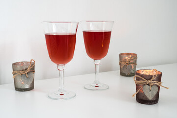 Close-up of couple of glasses with wine and candles with wooden hearts on table. Romantic composition. White background.