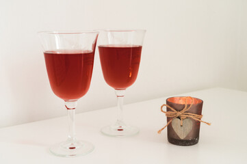 Close-up of couple of glasses with wine and candle with wooden heart on table. Romantic composition. White background.