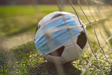 Naklejka premium Soccer Ball in Medical Mask on Stadium Green Grass. Ball in Goal Net. Football Competitions Stopped