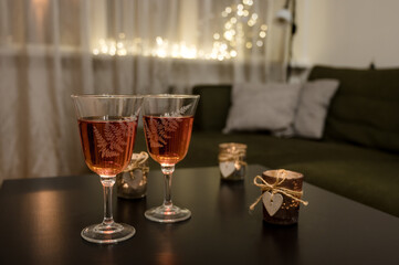 Couple of glasses with wine and candle with wooden heart on black table. Romantic composition. Modern interior. Close-up. Bokeh lights.