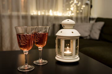 Couple of glasses with wine and candle in lantern on black table. Romantic composition. Modern interior. Close-up. Bokeh lights.