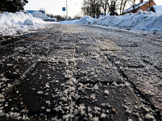 Salt grains on icy sidewalk surface in the winter