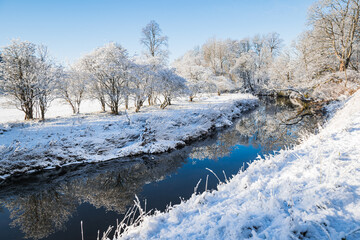 Winter in Pollok Country Park, Glasgow, Scotland, with snow-covered trees reflecting in the river.