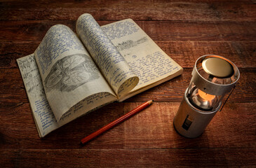 Vintage expedition journal on a picnic table with a candle lantern. Travel log from paddling trip across north eastern Poland in August 1974 - handwriting and drawing in pencil.