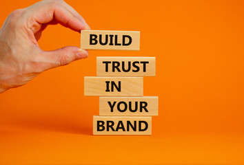 Success business process symbol. Wood blocks stacking as step stair on orange background, copy space. Businessman hand. Words 'build trust in your brand'. Business and trust brand concept.