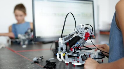 Smart schoolboy sitting at the table and constructing a robotic device in a school lesson - Powered by Adobe