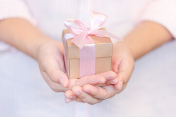 Female hands holding a gift wrapped with pink ribbon