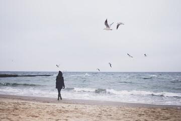 Beautiful woman walking on the beach with seagulls in winter time.