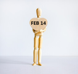 February 14 valentines day symbol. Wooden model of a human holding a wooden heart with words 'Feb 14'. Beautiful white background, copy space. February 14 Valentines day concept.
