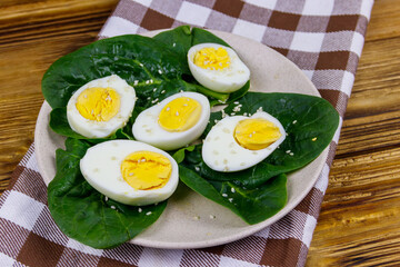 Boiled eggs with fresh spinach leaves and sesame seeds on wooden table