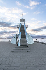Symmetric staircase at Nallikari lighthouse in Oulu, Finland. Scenic evening skyline over deep blue Baltic sea with stunning clouds at sunset. Maritime tower at the end of stone paved pier-upright