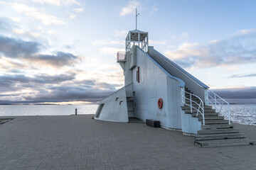Nallikari lighthouse in Oulu, Finland. Scenic evening skyline over deep blue Baltic sea with stunning clouds at sunset. Maritime tower at the end of stone paved pier.