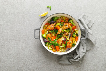 Chicken drumsticks roasted with vegetables in cast iron pan on kitchen table. Top view