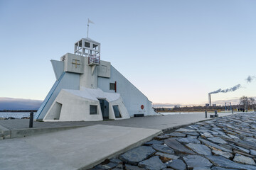 side view of Nallikari lighthouse in Oulu, Finland at Baltic sea. Maritime tower at the end of stone paved pier with smoke of a factory in the background. cloudless sky