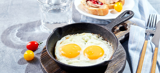 Fried eggs. Fried eggs from two eggs in cast-iron pan with cherry tomatoes and microgreens, toast and cup of coffee. Sunny morning breakfast concept