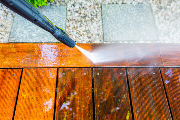 cleaning the terrace with a pressure washer - high-pressure cleaner on the wooden surface of the...