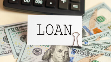 The word Loan is written in a notebook next to the bills and a black calculator. Business concept