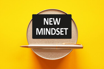 NEW MINDSET - words on a black sheet on a yellow background with round metal stand and metal writing pen. Business, finance and education concept