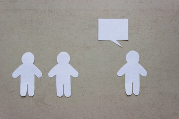 Silhouettes of people cut from white paper on a beige background. A couple of people stands in front of one person who is speaking (speech-bubble). 