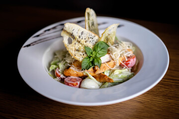 Classic Caesar salad with grilled chicken breast and half of egg in white ceramic plate. Served old dark blue wooden background.