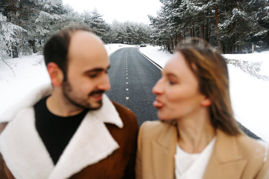 pareja joven abrigada feliz abrazándose sacando la lengua en el exterior en bosque en un día frio de invierno