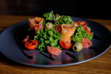 Fresh salad with salmon, tomatoes, lettuce, grapefruit, on a black plate