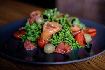 Fresh salad with salmon, tomatoes, lettuce, grapefruit, on a black plate