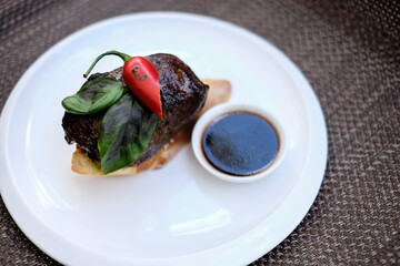 grilled beef fillet medallions on noodles with red hot chili pepper and salad leaf on white plate