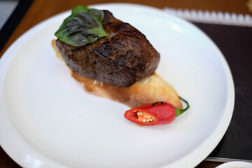 grilled beef fillet medallions on noodles with red hot chili pepper and salad leaf on white plate