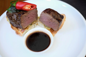 grilled beef fillet medallions on noodles with red hot chili pepper and salad leaf on white plate