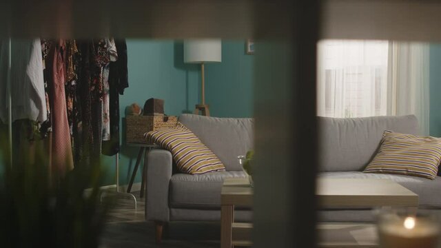 Young girl in jeans, a brown sweater enters the room, takes a mobile phone and a red apple from the table, sits on the couch