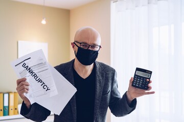 A man in a protective mask with a bankruptcy document and a calculator in his hand during a...