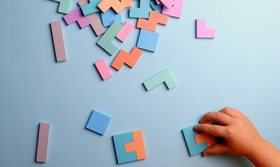 wooden puzzle in the shape of geometric shapes on a blue background with a child's hand selective focus.
