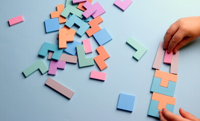 wooden puzzle in the shape of geometric shapes on a blue background with a child's hand selective focus.