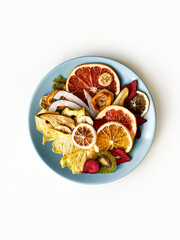Mixed dried fruit chips in round ceramic plate on white isolated background. Top view, flat lay.