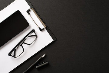 Flatlay photo of office accessories clipboard with blank pages telephone eyewear and pen isolated black background