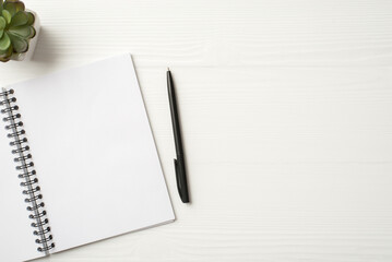 Flat lay view photo of open note pad on spiral with clear pages and black pen for writing essay isolated white wooden backdrop with copy space