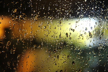 Water rain drops on a window with orange and green light from behind 