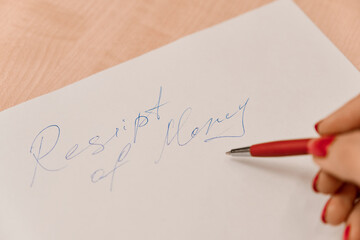 Hands of  young white woman with neat red manicure dressed in white blouse writing receipt of money on paper. Copy Space. Concept of real estate agent job