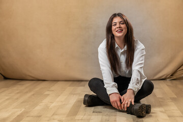 guapa joven sentada en habitación sonriendo con camisa blanca.