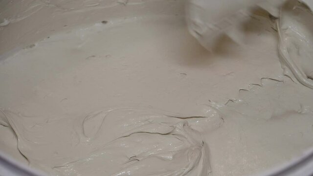 Stir the gray putty with the White Bucket. Human hand. Iron spatula. Artificial light. Preparation of the base. Internal construction and finishing works. Home repairs. Close-up.