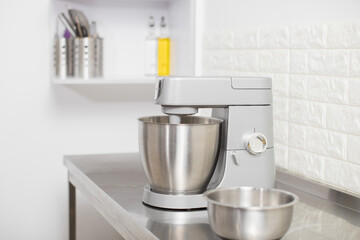 Small Electric Kitchen Appliances. Modern silver kitchen stand mixer in light cozy confectionery. A closeup of Multi-Task Blender mixing dough, and Stainless Steel bowl on the table
