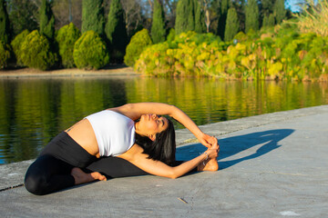 Fototapeta na wymiar Young attractive sportswoman practicing yoga, doing the exercise Revolved Head to Knee Forward, Parivrtta Janu Sirsasana pose, exercising, in the morning and a lake in the background.