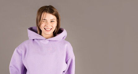 Fototapeta premium Close up portrait of happy young woman smiling and winking against gray wall
