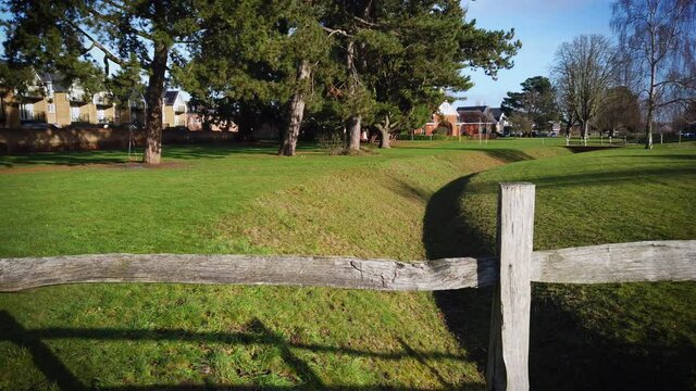 View beside rough wooden fence above the drainage canal. Beautiful green but empty park in UK during the covid 19 pandemic.