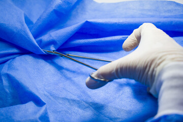 Closeup of a surgeon wearing a latex glove and holding forceps against a blue background